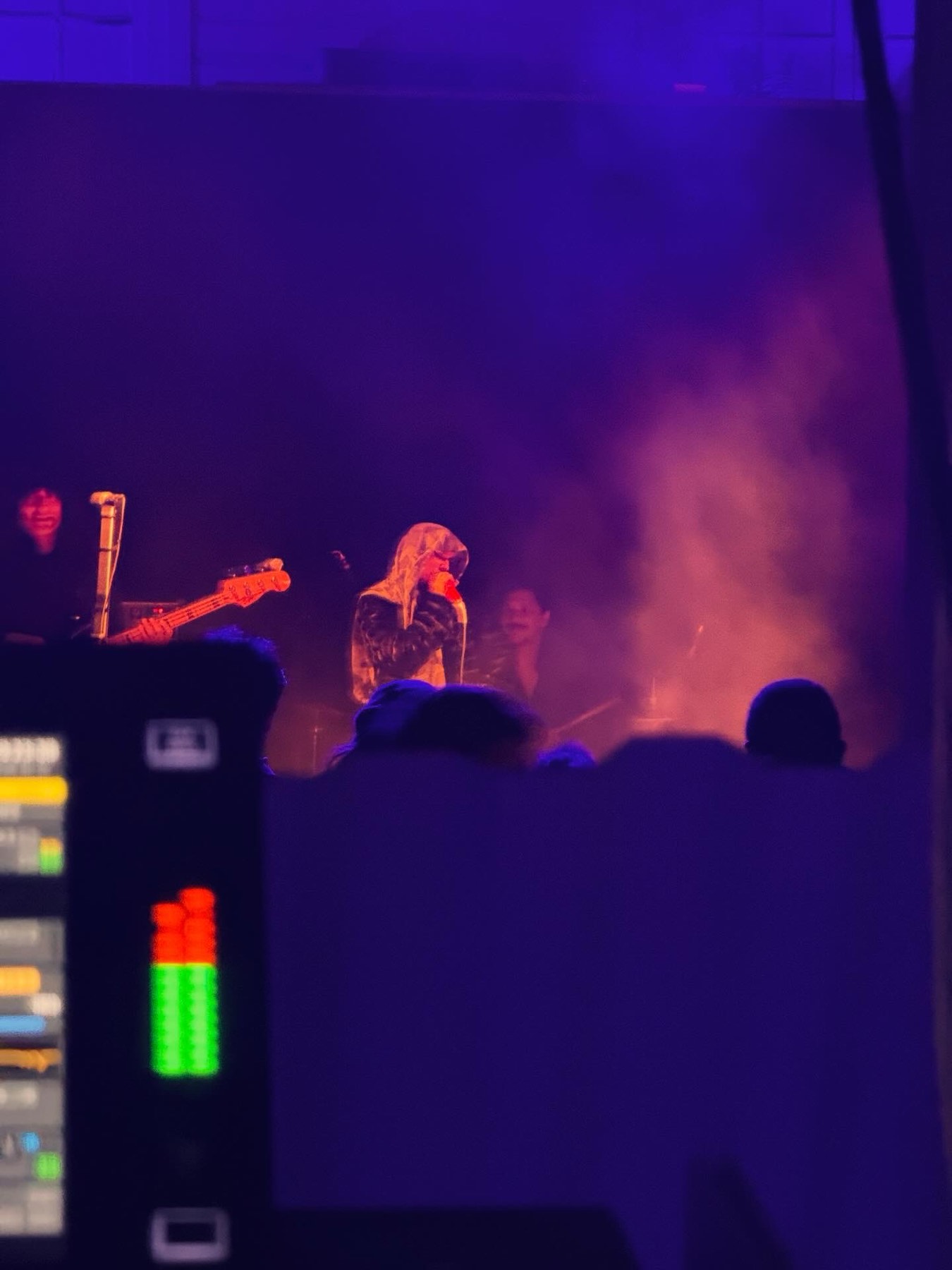 View of a band on stage from the front-of-house mix position, console meters in the foreground