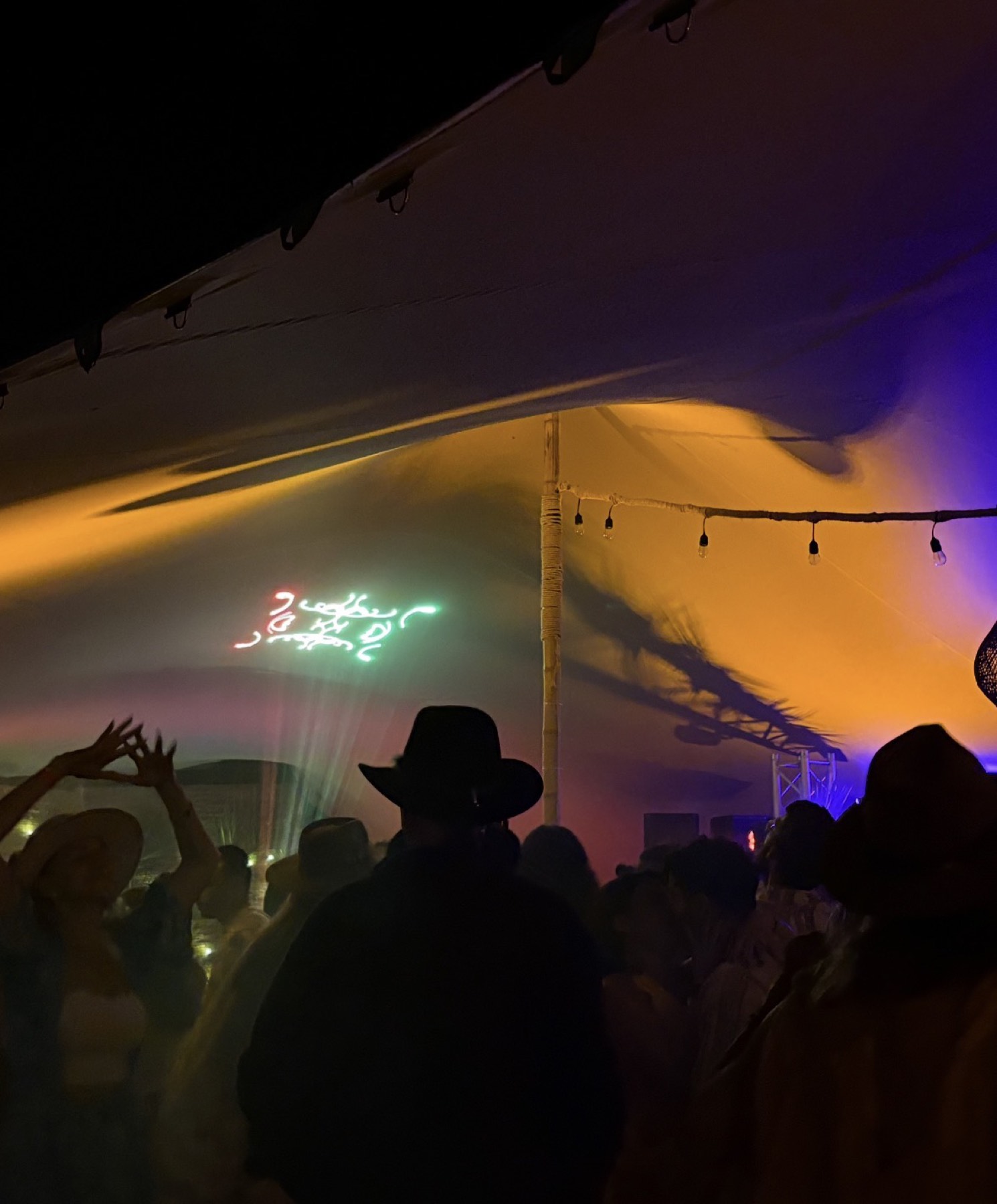 Crowd dancing under a tent with laser and color wash
